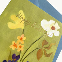Close-up of gold foil Happy Birthday lettering over yellow and white flowers on a green card