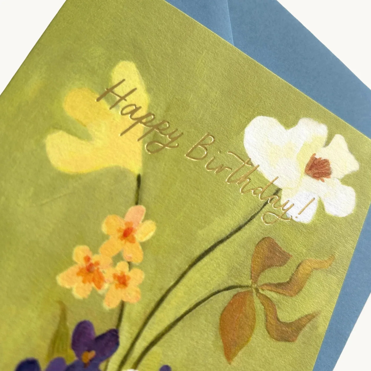Close-up of gold foil Happy Birthday lettering over yellow and white flowers on a green card
