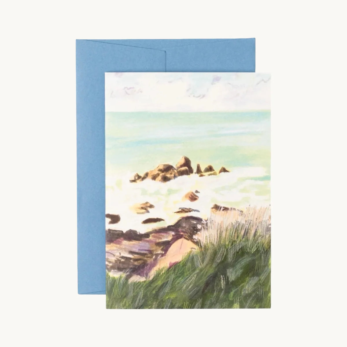 Greeting card of rocks in turquoise surf seen over windswept green grass, with a blue envelope