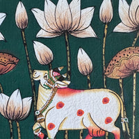 Close-up of a decorated white cow with orange markings among white lotus flowers and gold-edged stems, on green cloth