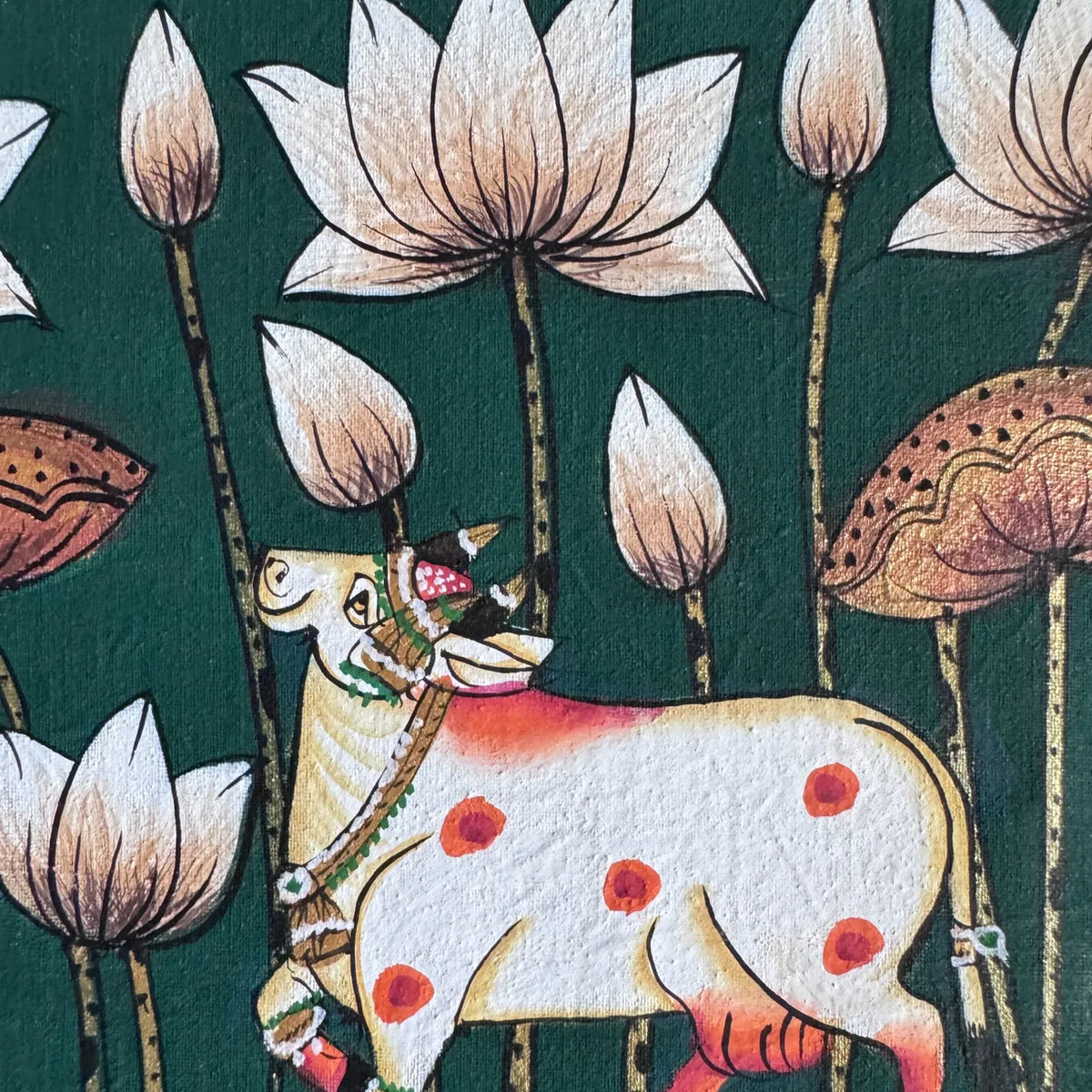 Close-up of a decorated white cow with orange markings among white lotus flowers and gold-edged stems, on green cloth