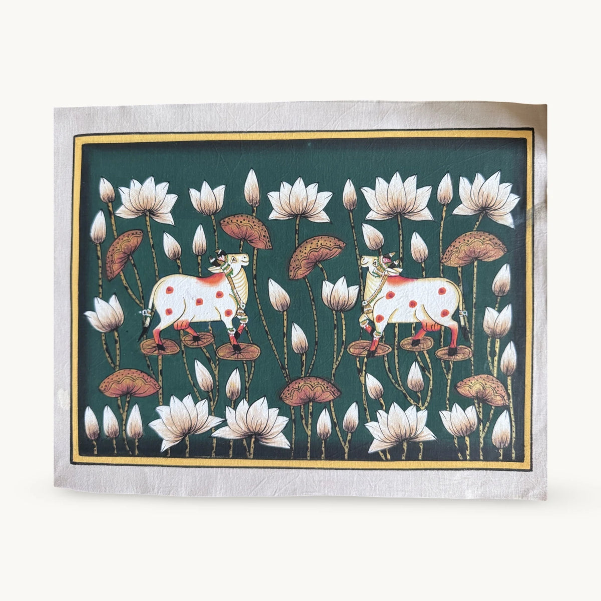 Original painting on cloth of two white cows with orange spots facing each other among lotus flowers and buds on a deep green ground with a yellow border