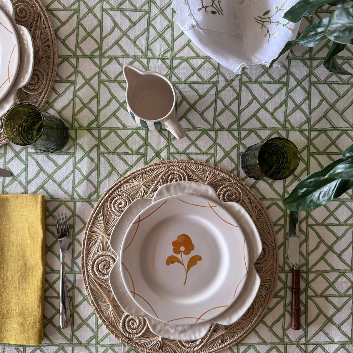 Cane Garden green lattice tablecloth with a floral plate on a rattan charger, mustard napkin and small jug