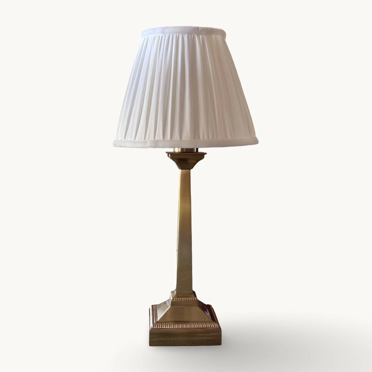The Voyage Dubai - Cordless Antique Gold Table Lamp with White Pleated Shade - Rechargeable iron table lamp. Front view on a cream background.