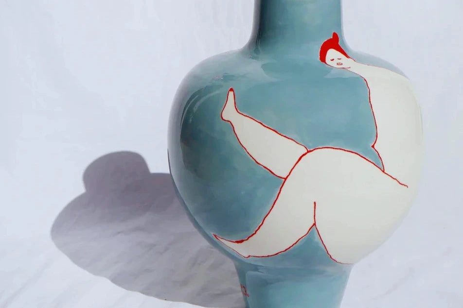 Laetitia Rouget Queen Blue Vase — hand-painted ceramic with reclining female figure in red, photographed against white linen.
