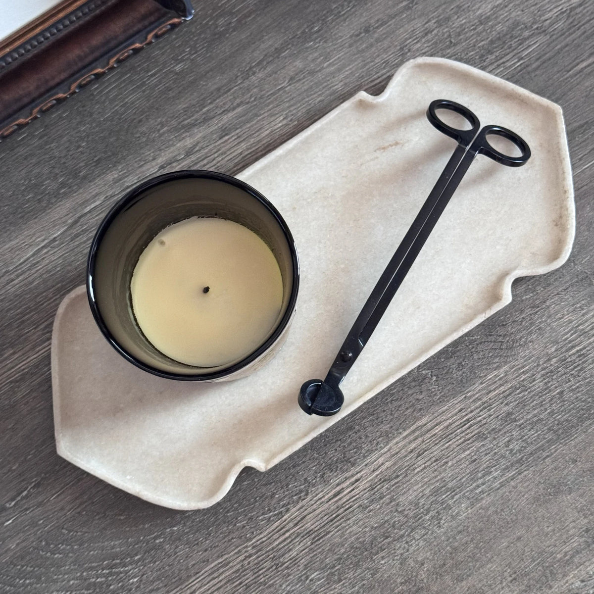Top view of the marble tray on a wooden table holding a candle and a black wick trimmer