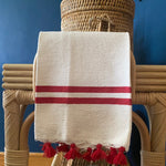 The Voyage Dubai - Made in Tangier Jibli Hand Towel - Red  Hand woven in Morocco from 100% pure cotton, the Jibli Hand Towel in double stripe is a great way to add a pop of colour to a guest bathroom, drinks cart or kitchen. The towels are finished with a fringe of pom poms and are made from a wonderfully soft yet highly durable handwoven cotton, making them perfect for everyday use.   Use as table napkins, tea towels or hand towels.