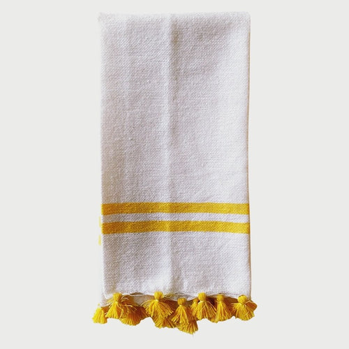 The Voyage Dubai - Made in Tangier Jibli Hand Towel - Yellow  Hand woven in Morocco from 100% pure cotton, the Jibli Hand Towel in double stripe is a great way to add a pop of colour to a guest bathroom, drinks cart or kitchen. The towels are finished with a fringe of pom poms and are made from a wonderfully soft yet highly durable handwoven cotton, making them perfect for everyday use. 
