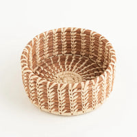 The Voyage Dubai. Handmade and designed by Mayan Hands artisan partners in Sololá, Guatemala this delicately woven pine needle and raffia bottle coaster adds a lovely touch to the table while protecting it from drips and stains.  It accommodates a standard bottle of wine.  The small basket also doubles as a little catchall by the front door or for your desk.  Handmade and fair trade.  Origin – Guatemala  Material - native grass, pine needles, raffia  Approximate Dimensions: 4.5" diameter x 2" high