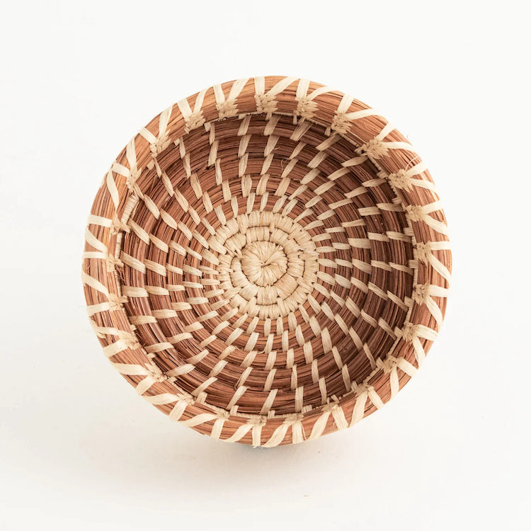 The Voyage Dubai. Handmade and designed by Mayan Hands artisan partners in Sololá, Guatemala this delicately woven pine needle and raffia bottle coaster adds a lovely touch to the table while protecting it from drips and stains.  It accommodates a standard bottle of wine.  The small basket also doubles as a little catchall by the front door or for your desk.  Handmade and fair trade.  Origin – Guatemala  Material - native grass, pine needles, raffia  Approximate Dimensions: 4.5" diameter x 2" high